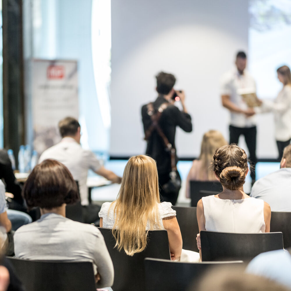 Award ceremony at a business event. Woman receiving an award on stage as people in a crowd are watching.